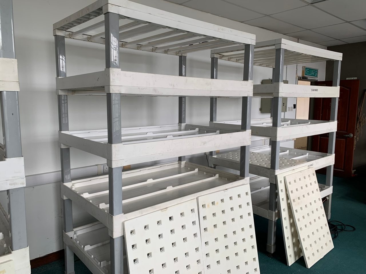Two white SANANBIO growing racks with several levels; white plant boards with rows of square holes lean against the lower shelves